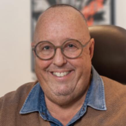 Lächelnder Mann mit Brille, kurzer Haarschnitt und braunem Pullover mit blauer Kragen.