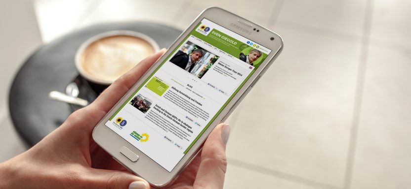 Ein Smartphone zeigt eine App-Oberfläche mit Nachrichten und Profilen. Kaffee steht daneben.